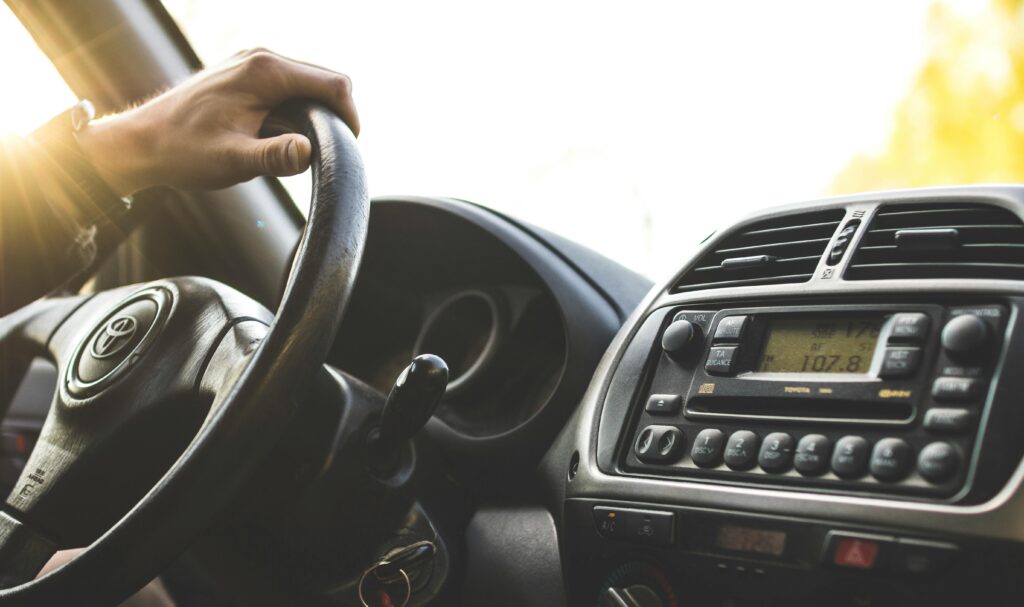 pexels-photo-1073031-1073031 Close-up of a hand on a steering wheel inside a car, dashboard visible.